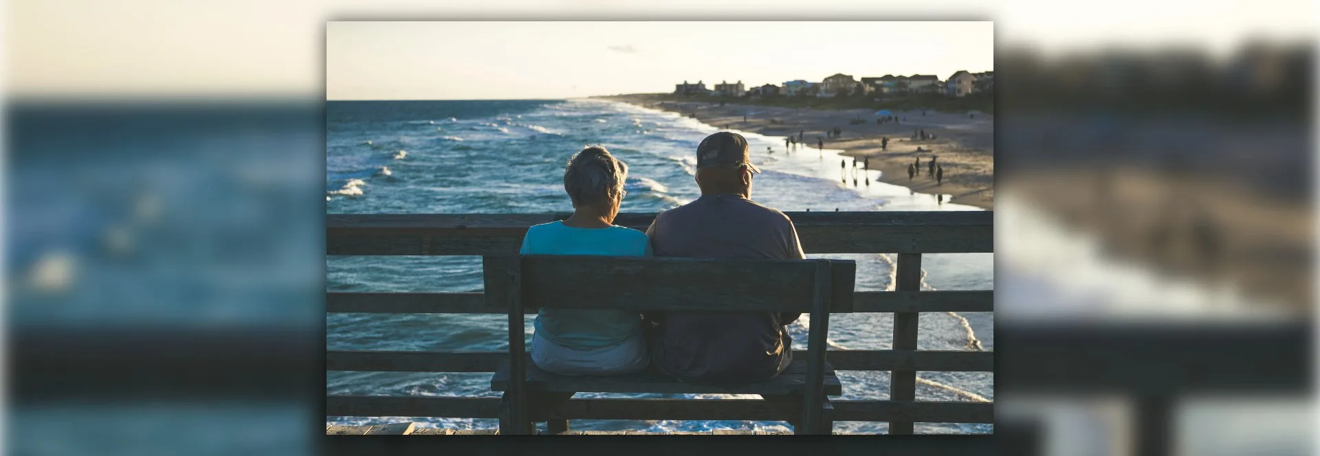 Couple de personnes âgées assis sur un banc en bois face à l'océan, le dos tourné, contemplant la Côte de Jade au coucher de soleil.